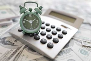 Clock sitting on a calculator and money to symbolize a financial deadline