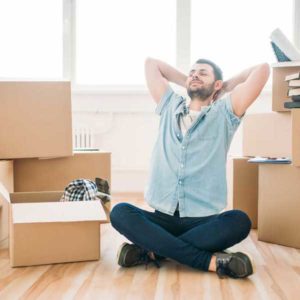 Man sitting cross-legged stretching in his new home among moving boxes